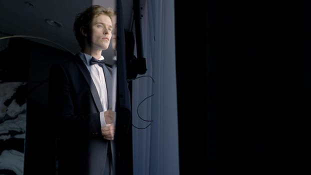 A worried groom man standing by the window. Action. Thoughtful attractive husband wearing suit before wedding ceremony