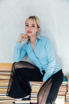 Beautiful fashionable female teacher sitting on stacks of books