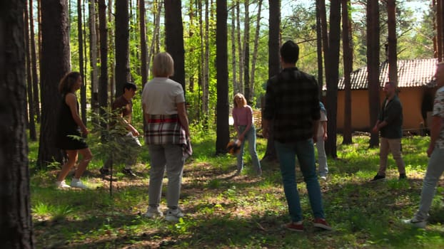 Tourists play volleyball in park. Stock footage. Vacationers at recreation center play volleyball in forest. People play volleyball in circle in park on sunny summer day.