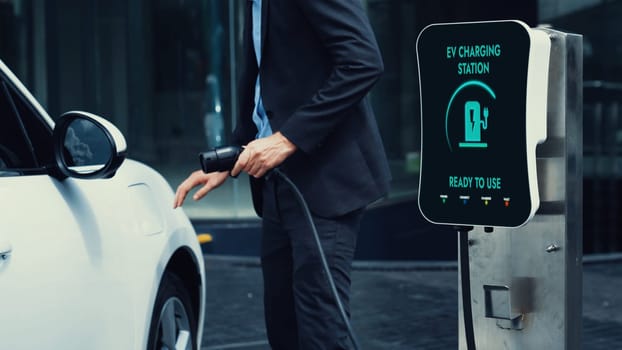 Businessman recharge his electric car from charging station at city center or public car park. Eco friendly rechargeable car using alternative clean energy in urban city lifestyle.Peruse