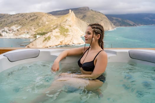 Take time for yourself. Outdoor swimsuit with mountain and sea views. A woman in a black swimsuit is relaxing in the hotel pool, admiring the view.