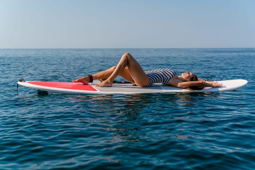 Sporty girl on a glanders surfboard in the sea on a sunny summer day. In a striped swimsuit, he lies on his back. Summer activities by Stortom by the sea.