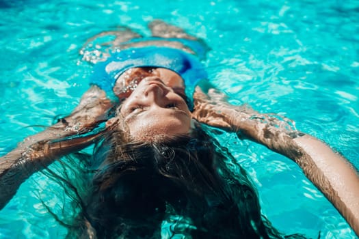 Woman relaxing swimming pool. Happy woman in a blue swimsuit floating in the pool, look form above.