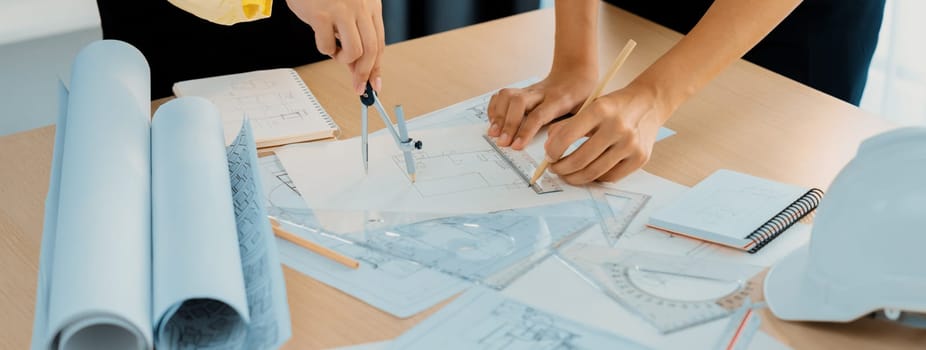 Professional architect team used divider measure during draft blueprint on table with architectural document, safety helmet and blueprint scatter around. Closeup. Focus on hand. Delineation.