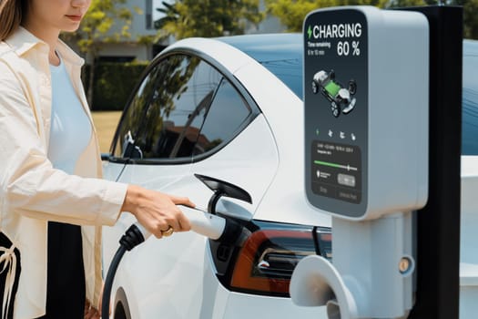 Young woman put EV charger to recharge electric car's battery from charging station. Alternative energy and rechargeable EV car for sustainable environmental friendly travel concept. Expedient