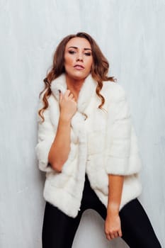 Portrait of a beautiful woman with hair curls in a white fur coat