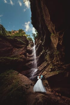 Couple in love on a waterfall. Honeymoon trip. Happy couple in the mountains, high angle view of the entire mountain waterfall.