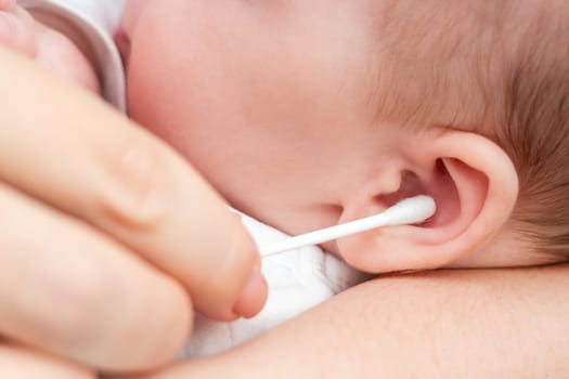 Mother meticulously cleans her newborn's ear with a soft cotton stick, ensuring comfort and