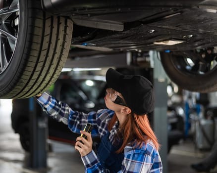 A female mechanic inspects a lifted car. A girl at a man's work