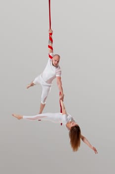 Gymnasts performance on a long red canvases. Attractive female and an athletic male in a light sport suits are doing acrobatic elements in a studio isolated on white background. Dancing in the air with love and balance.