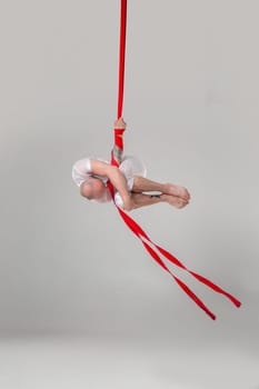 Gymnast performance on a red canvases. Athletic person in a light sport suit is doing an acrobatic elements in a studio isolated on white background. Dancing in the air with balance.