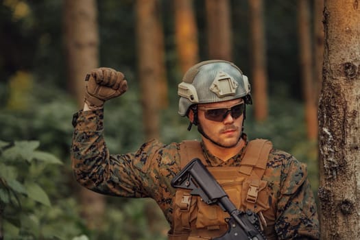 Modern warfare soldier officer is showing tactical hand signals to silently give orders and alers for squad team forest enviroment.