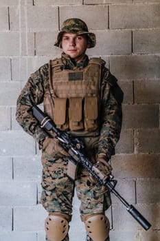 A soldier in uniform stands in front of a stone wall in full war gear preparing for battle.