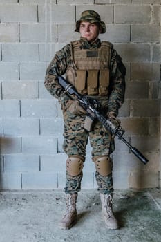 A soldier in uniform stands in front of a stone wall in full war gear preparing for battle.