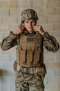 A soldier in uniform stands in front of a stone wall in full war gear preparing for battle.