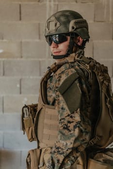 A soldier in uniform stands in front of a stone wall in full war gear preparing for battle.