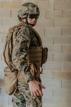 A soldier in uniform stands in front of a stone wall in full war gear preparing for battle.