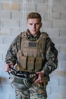 A soldier in uniform stands in front of a stone wall in full war gear preparing for battle.