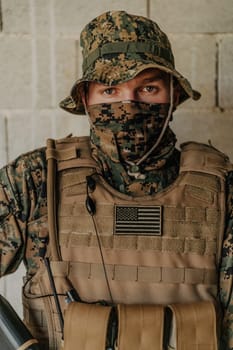 A soldier in uniform stands in front of a stone wall in full war gear preparing for battle.