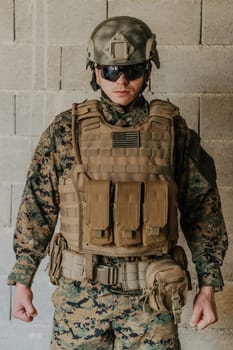 A soldier in uniform stands in front of a stone wall in full war gear preparing for battle.