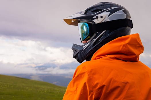 a man in a helmet and protection stands with a bicycle. on a green hill among the mountains during a break between riding off the road.