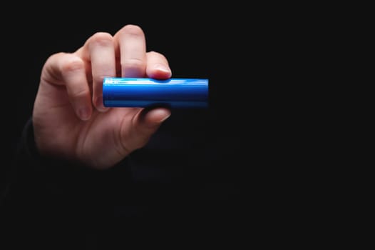 Lithium-ion battery for power in a human hand, on a black background. Woman's hand showing a battery, close-up, mockup.