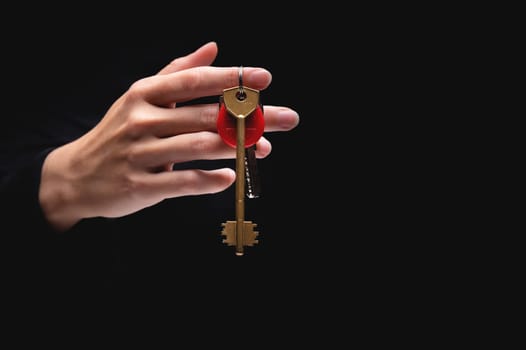 A woman's hand holds keys with a round red keychain on a black background. The hand gives the keys from the darkness.