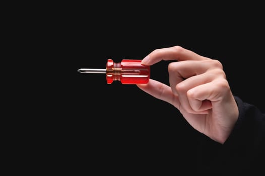 A small screwdriver with a red handle in a female hand, on a black background, gives the tool from the side