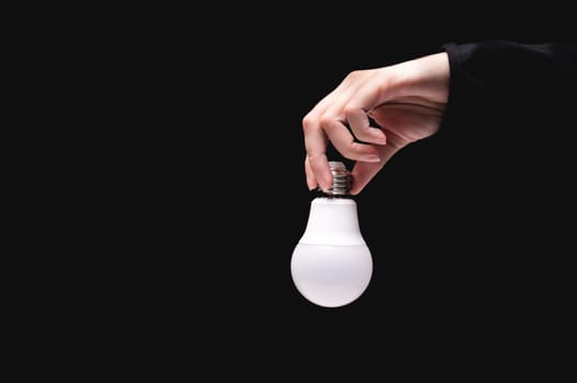 A hand holds an LED light bulb on a black background. Using an economical and environmentally friendly light bulb concept. Idea. Energy saving lamp in a woman's hand