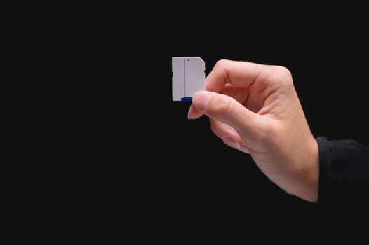Close-up of a woman showing a memory card. Hand holding a blank SD card in white on a black background.