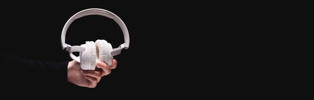 white headphones in a woman's outstretched hand on a dark background, banner for advertising.