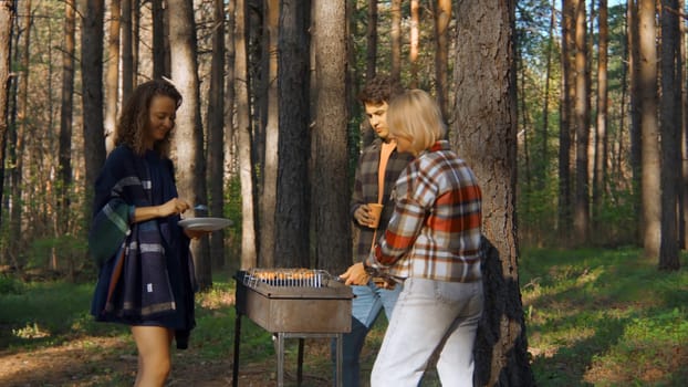 Friends cook grilled meat in forest in summer. Stock footage. Beautiful friends are relaxing in nature with barbecue in forest. Relaxing with friends in nature with barbecue on sunny summer day.