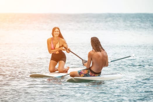 Sea woman and man on sup. Silhouette of happy young woman and man, surfing on SUP board, confident paddling through water surface. Idyllic sunset. Active lifestyle at sea or river