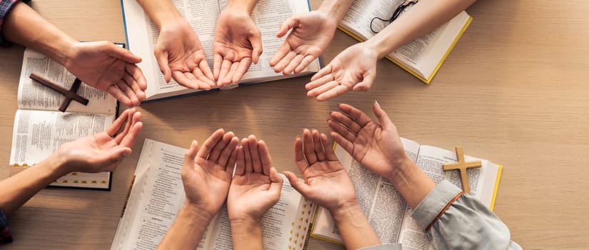 Cropped image of diversity people hand praying together at wooden church on bible book. Group of believer hold hand together faithfully. Concept of hope, religion, faith, god blessing. Burgeoning.