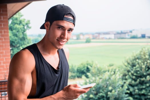 A man in a black tank top holding a cell phone, outdoor, looking at camera smiling