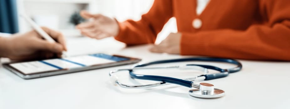 Focused stethoscope on office desk with blurred background of patient attending to doctor appointment at clinic or hospital discussing medical treatment or examining symptoms. Panorama Rigid