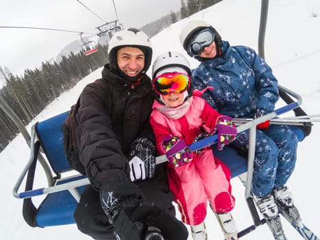 Skiing, ski lift, ski resort - happy smiling family skiers on ski lift making selfie.