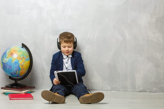 Cheerful little boy holding digital tablet against gray background. School concept. Back to School.