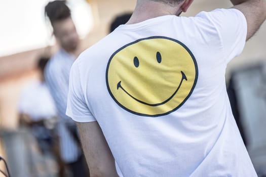 A person seen from the back wearing a shirt with a large, cheerful smiley emoticon.