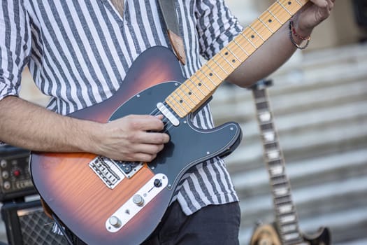 Close-up of a musician's hands playing the guitar during a live daylight performance.