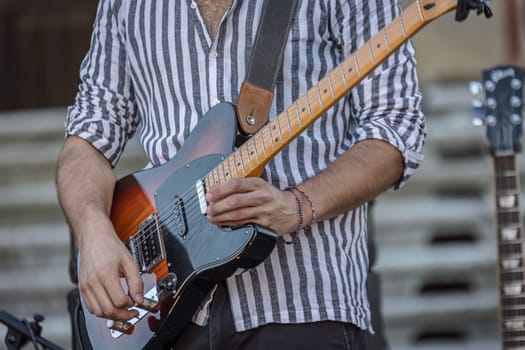 Close-up of a musician's hands playing the guitar during a live daylight performance.