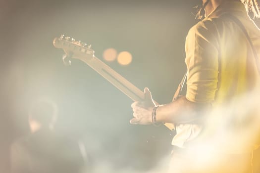 A guitarist seen from behind, playing in a foggy, atmospheric night concert setting.