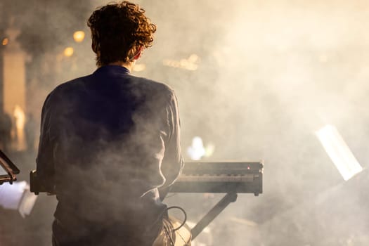 A pianist seen from behind, playing in a night concert with a mystical foggy atmosphere.