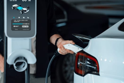 Young man travel with EV electric car to shopping center parking lot charging in downtown city showing urban sustainability lifestyle by green clean rechargeable energy of electric vehicle innards