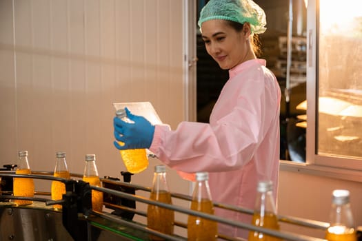 Woman technician in uniform checks bottles on conveyor using laptop. Quality control manager ensures drink's perfection. Science meets manufacturing as technology-driven control is maintained.
