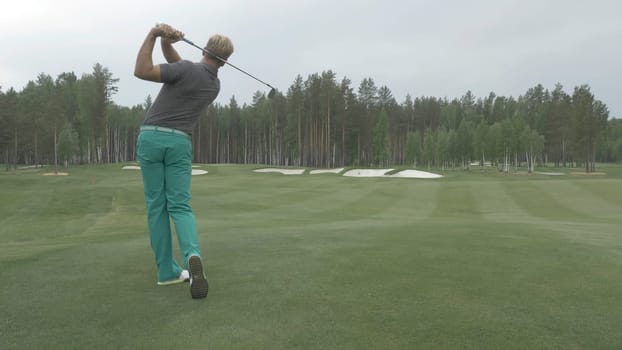 Golfer Hitting Ball with Club on Beautiful Golf Course. Golfer hits an fairway shot towards the club house. Man hitting driver on a golf course in the sun. Professional male golf player f