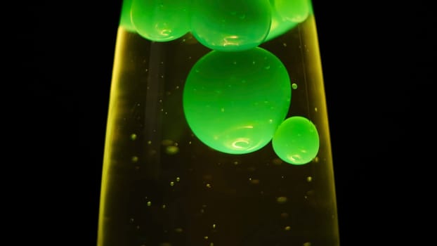 Close up view of green lava lamp isolated on black background. Unusual lamp with dim light and moving green bubbles creating relaxing atmosphere.