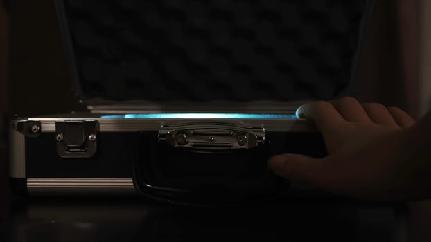 Close up of female hands opening silver metal suitcase with locking system. Opening aluminum carrying case to find shining mysterious object inside.