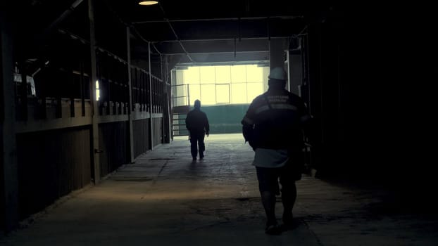 Rear view on silhouette of industrial workers walking on production hall on metallurgical plant. Following Shot of Engineers Walking Through Heavy Industry Manufacturing Factory.