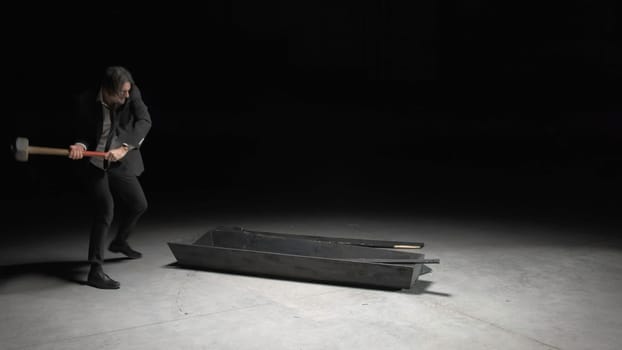 Man with sledgehammer. Stock footage. Man in dark room breaks wooden box out of anger. Man with hammer breaks wooden box.